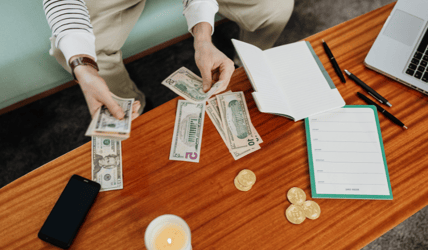 A person counts money on a coffee table, with a planner and notebook laid to the side.